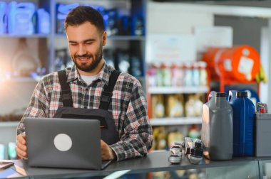 Gülümseyen tamirci ya da tezgahtar dizüstü bilgisayara bakıyor, bir oto yedek parça dükkanında envanter ya da siparişleri yönetiyor