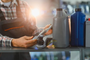 Tamirci süspansiyon parçası tutuyor ve rafında motor yağı ve araba aküsü olan bir oto yedek parça mağazasında çalışıyor.