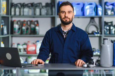 Bir oto yedek parça mağazasında cep telefonu ve dizüstü bilgisayar kullanarak tezgahın arkasında duran bir erkek tezgahtar.