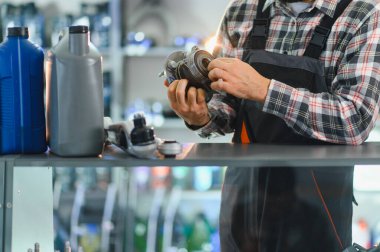 Erkek tamirci yeni bir araba tekerleği gövdesini dikkatle inceliyor, bir araç servis garajında duruyor. Rafta kayganlaştırıcı yağlar