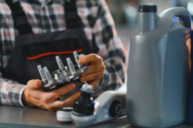 Tamirci araba tekerleği merkezi ve diğer yeni otomobil parçaları tutuyor, atölyede araç bakımına veya tamirine hazırlanıyor