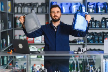 Erkek tamirci oto yedek parça dükkanında duruyor, karşılaştırma için motor yağı şişeleri tutuyor, kaliteli araç servisi sağlıyor