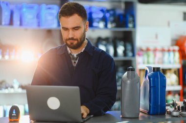 Otomotiv yedek parça ve tamirhanesinde dizüstü bilgisayar kullanan üniformalı bir erkek işçi.