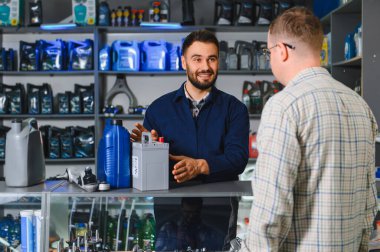 Araba aküleri ve motor yağı hakkında müşteriye tavsiye veren otomobil parçaları satıcısı, modern bir araç hizmet dükkanında sergileniyor.