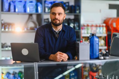 Tezgahta dizüstü bilgisayar, pil ve motor yağıyla duran ve yedek parça satan bir mağaza çalışanı.