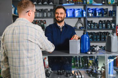 Satıcı, oto yedek parça mağazasındaki bir müşteriye hizmet ve tavsiye sunan bir araba aküsü ve motor yağı tavsiye eder
