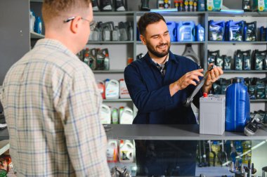 Tamirci bir oto yedek parça dükkanında müşteriye yardım ediyor, bir araç parçası tutuyor ve araba bakımı seçeneklerini tartışıyor