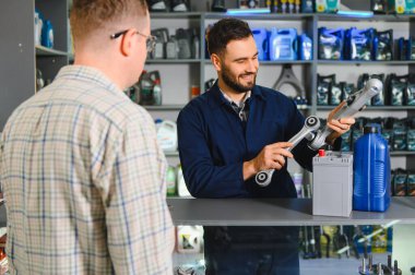 Otomobil parçaları satıcısı üniforma giyen, müşteriye yardım eden, perakende satış mağazasında bir kontrol kolu tutan,