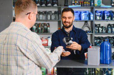 Otomobil parçası satan bir mağazadaki müşteriye otomotiv parçaları sağlayan servis çalışanı, araba bakım malzemeleri sunuyor.