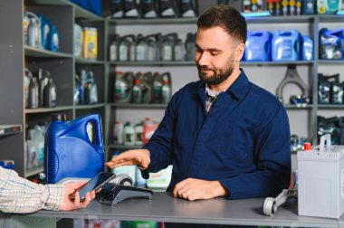 Müşteri, oto yedek parça tezgahında ulaşılamayan ödemeler için akıllı telefon kullanıyor, atölyede motor yağı ve araba aküsü satın alıyor