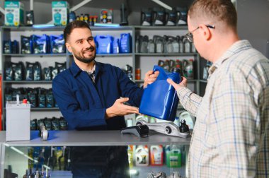 Gülümseyen tamirci, bir otomotiv mağazasında araba motor yağını seçen bir erkeğe yardım ediyor.