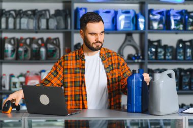 Otomobil parçaları mağazasında çalışan bir adam, motor yağı şişelerini barkod tarayıcı ile tarıyor ve envanter için bir dizüstü bilgisayar kullanıyor.