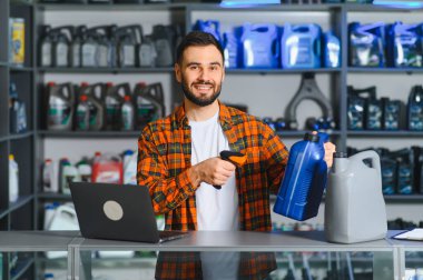 Otomobil dükkanında çalışan gülümseyen bir adam barkod tarayıcı ve dizüstü bilgisayarla motor yağı stoklarını kontrol ediyor.