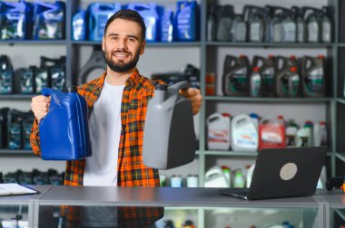 Gülümseyen satıcı motor yağı kutularını tutuyor, araba bakımı ve otomobil servisi için yağlama ürünleri sunuyor.