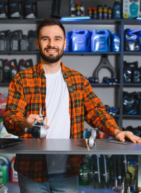 Genç pazarlamacı elinde yağ bidonuyla tezgahta duruyor, bir otomotiv dükkanında hizmet ve ürün sunuyor.