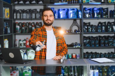 Otomotiv tezgahında çalışan kareli gömlekli bir satıcı müşteriye bir araç parçası sunuyor.