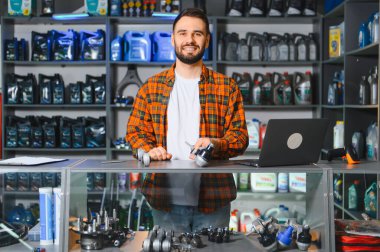 Otomotiv dükkanında satıcı olarak çalışan mutlu sakallı bir adam. Elinde yedek parça var ve kameraya gülümsüyor.