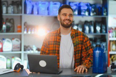 Gülümseyen adam oto yedek parça mağazasının arkasında duruyor, envanter yönetimi ve müşteri hizmetleri için dizüstü bilgisayar kullanıyor.