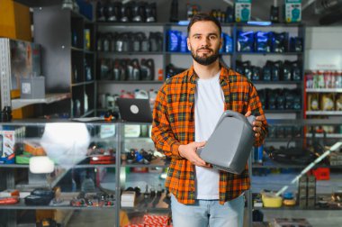 Bir araba parçası dükkanında elinde motor yağı tüpüyle kameraya bakan bir adam. Araba bakımı için alışveriş.