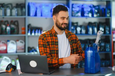 Satış elemanı mavi bir kayganlaştırıcı konteynır üzerinde barkod tarayıcı kullanıyor, bir otomotiv parçası mağazasında, envanteri yönetiyor.