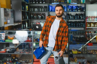 Araba yağı konteynırları tutan adam, bir perakende dükkanında otomobil ürünleri ve bakım malzemeleri alışverişi yapan adam.