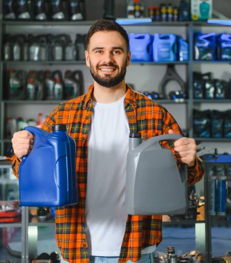 Çekici bir adam gülümsüyor, iki tip motor yağı arasında seçim yapıyor, bir perakende dükkanından araba bakım malzemeleri alıyor.