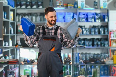 Otomotiv malzemeleri satan bir dükkanda farklı motor yağı ürünlerini karşılaştıran mutlu bir tamirci. Araç bakımı konusunda uzman tavsiyesi