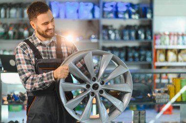Gülümseyen tamirci otomotiv veya tamirhanede araba alaşımlı tekerleği kontrol ediyor, müşteriye danışıyor.