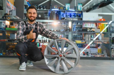 Tulum giymiş, elinde alaşım tekeri olan ve otomotiv parçaları satan mutlu bir araba servis elemanı.