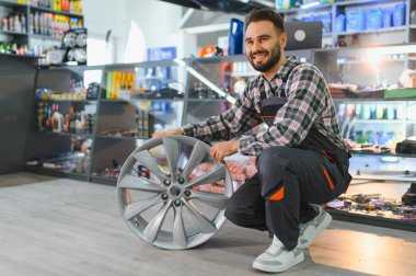 Araba alaşımı tekerleği tutan gülümseyen profesyonel işçi, satış ve bakım için bir otomotiv atölyesinde duruyor.