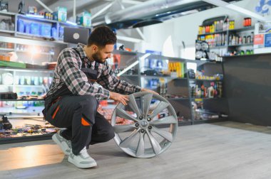 Araba tamircisi modern bir alaşım araç tekerleğini inceliyor, bir otomotiv tamirhanesinde lastik kurulumuna kalite ve hazırlık sağlıyor.