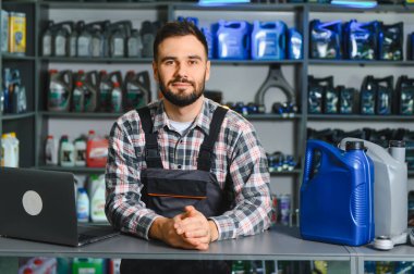 Otomobil tamircisi tezgahın arkasında duruyor, otomobil parçaları ve motor yağı kutularını gösteriyor. Hizmet ve bakım sağlanıyor