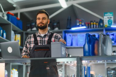Otomotiv yedek parça ve aksesuar dükkanında çalışan, elinde araba aküsü olan ve dizüstü bilgisayar kullanan bir erkek çalışan.