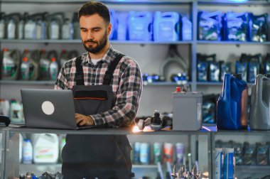 Otomobil servis danışmanı kasada dizüstü bilgisayarda çalışıyor, siparişleri yönetiyor ve modern bir araba parçası mağazasında stok yapıyor.