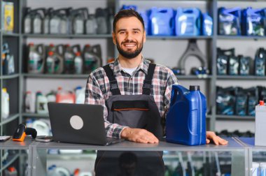 Tamirci tezgahta duruyor, gülümsüyor, araba bakım ürünleri için müşterilere yardım ediyor.