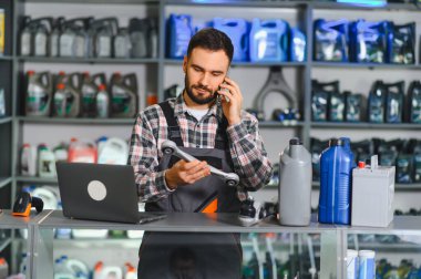Bir oto yedek parça mağazasında satış elemanı otomotiv ürünleriyle çevrili bir telefonla konuşurken araba süspansiyon bölümünü inceliyor.