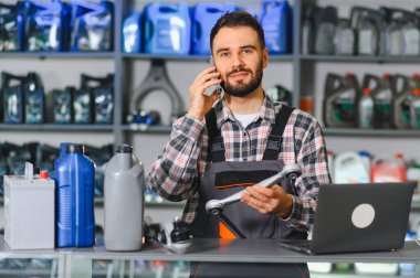 Otomobil servis teknisyeni bir tamircide araba parçası tutan bir müşteriyle cep telefonuyla iletişim kuruyor.