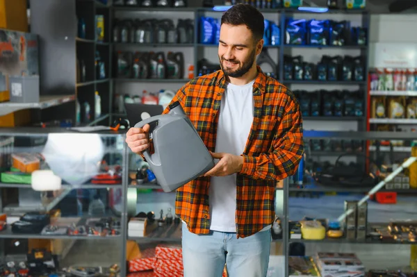 Ekose gömlekli gülümseyen adam modern oto yedek parça mağazasında araba bakımı sırasında motor yağı seçiyor.