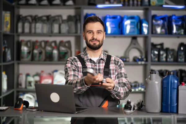 Tamirci, yeni araba parçası sunuyor. Bir tamirhanede dizüstü bilgisayar ve motor yağı ekranıyla çalışıyor.