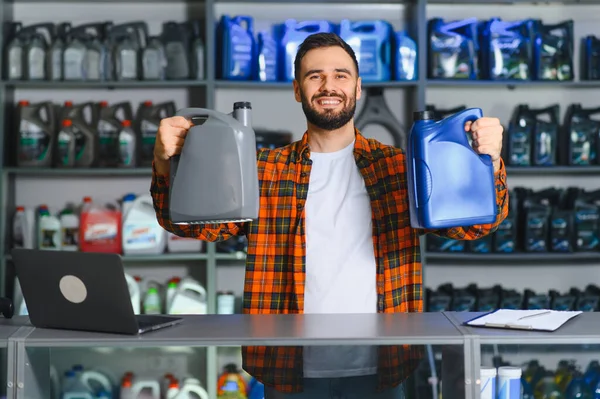 Araba parçaları satan bir dükkanda elinde iki kutu motor yağı tutan ve gülümseyen bir erkek işçi. Araba bakımı için kayganlaştırıcı satılıyor