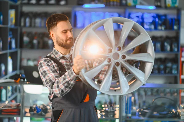 Otomobil tamircisi, parlak aydınlatılmış bir araba tamir atölyesinde kalite denetimi için yeni bir alaşım tekerleğini dikkatlice inceliyor.