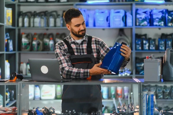 Oto yedek parça dükkanında çalışan bir adam elinde bir şişe motor yağı tutuyor. Otomotiv ürünleri satma ve danışmanlık