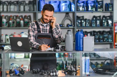 Gülümseyen tamirci bir tezgahta notlar alırken servis hakkında konuşuyor ve akıllı telefondan bileşenler sipariş ediyor.