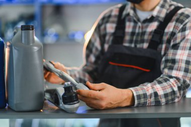 Otomobil servis teknisyeni yeni araba süspansiyon bölümünü bakım için tutuyor, motor yağı kapları da rafta.