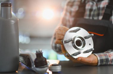 Otomotiv tamircisi yeni bir tekerlek merkezi ve taşıyıcı parçası tutuyor, diğer araba parçaları da atölye masasında.