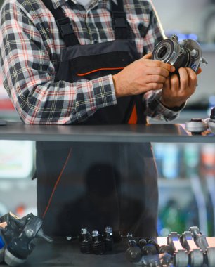 Tamirci araba servisi atölyesindeki yeni tekerlek merkezini inceliyor. Parçalar otomobil tamiri ve bakım için hazır.