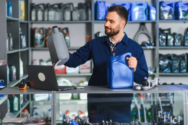 Bir araba atölyesinde ya da otomotiv hizmet merkezinde dururken iki motor yağı şişesi tutan üniformalı bir erkek işçi.