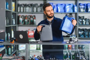 Tamirci, bir atölyede veya perakende mağazasında farklı motor yağı şişelerini karşılaştırarak, bakım için araba sıvısı sunuyor