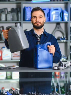 Otomotiv yedek parça ve aksesuar dükkanında çalışan, farklı türde motor yağı sunan erkek tamirci veya satıcı