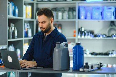Profesyonel servis elemanı bir dizüstü bilgisayar üzerinde çalışıyor, bir atölyede envanter ve otomobil parçaları ve motor yağı siparişlerini yönetiyor.